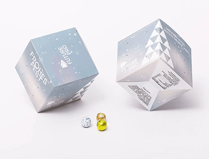 Zwei Adventskalender Cube ruhen auf ihren Kanten, vor zwei Schokoladenkugeln.