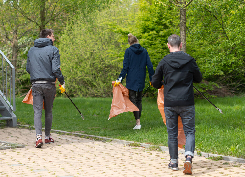 Team versammelt sich zum Aufräumtag im Park mit Müllsäcken und Zangen.