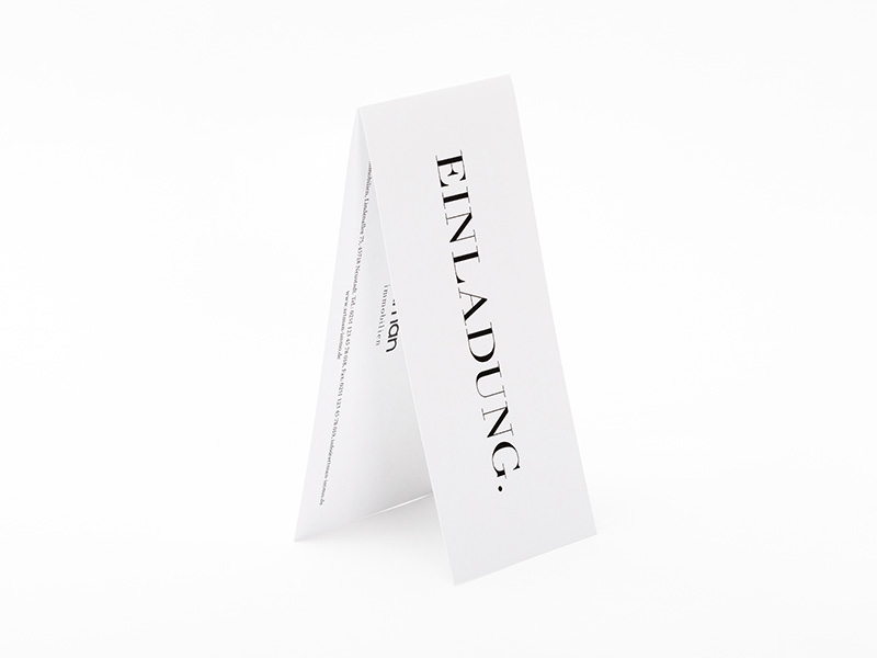 Eine zum Dach aufgestellte Grußkarte in weiß mit der Aufschrift Einladung.