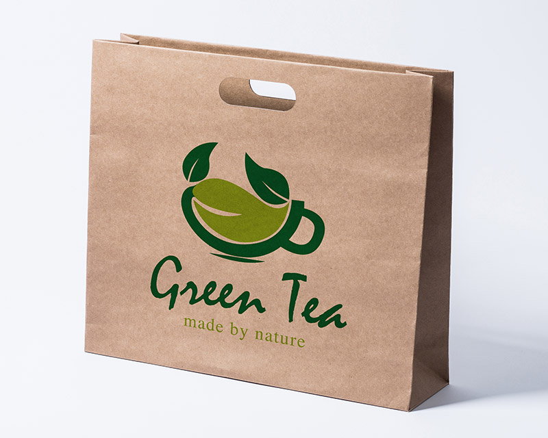 Die Abbildung zeigt eine ca. 20 Grad nach links gedrehte Papiertasche aus braunem Kraftpapier mit einem zweiarbig-grünem Logo in der Mitte platziert.