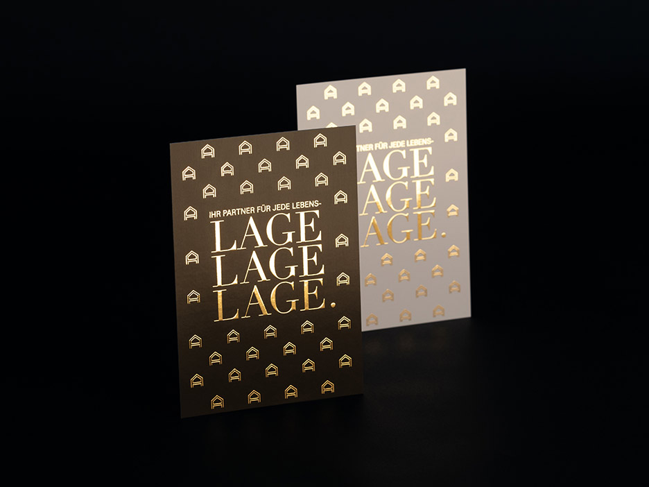 Zwei versetzt zueinander stehende Postkarten eines Immobilienunternehmens mit kleinen in haptisch goldfarbener Folie partiell veredelten Häuschen auf schwarzem Hintergrund