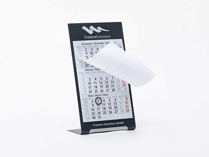Die Abbildung zeigt einen Tischkalender Metall, bei dem das oberste Kalenderblatt nach oben gerollt wurde.